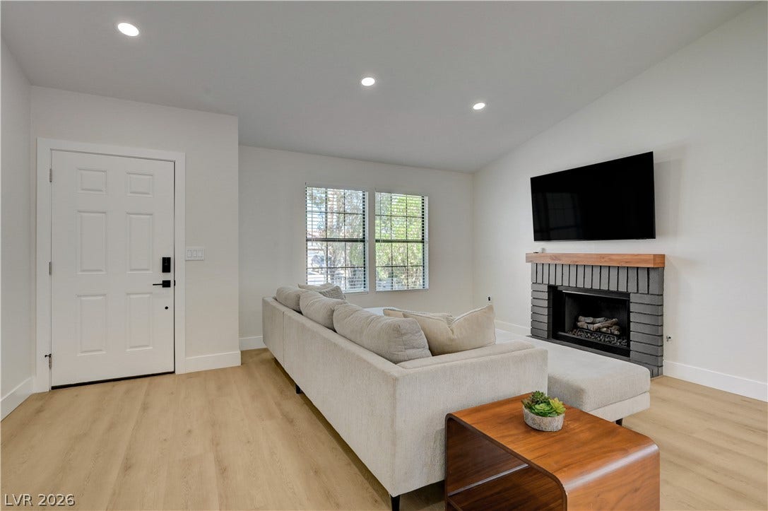 3131 White Rose Way, Henderson, NV 89014 The living room boasts a contemporary fireplace with a sleek hearth and light wood mantel, complemented by light hardwood flooring.