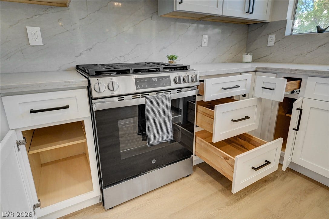 3131 White Rose Way, Henderson, NV 89014 A well-appointed kitchen showcasing a sleek stainless steel range and ample white cabinetry with contrasting dark pulls.