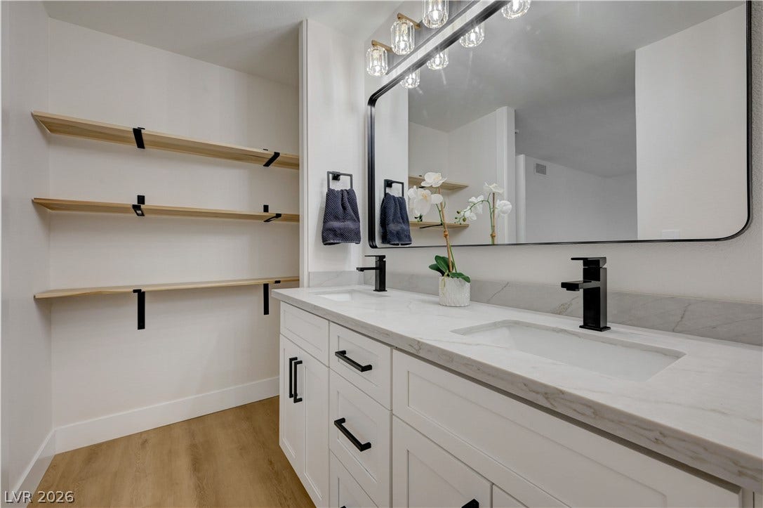 3131 White Rose Way, Henderson, NV 89014 Double vanities with sleek black fixtures and open shelving enhance this contemporary bathroom's functional elegance.