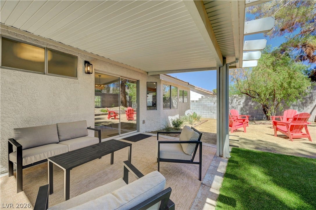 3131 White Rose Way, Henderson, NV 89014 A spacious covered patio invites relaxation, overlooking a xeriscaped yard with vibrant Adirondack chairs and verdant artificial turf.