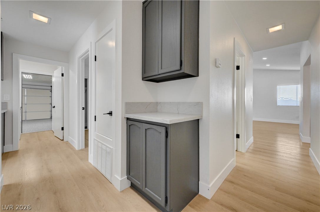 3131 White Rose Way, Henderson, NV 89014 A well-lit hallway with natural wood flooring leads to various rooms, including a visible garage space.