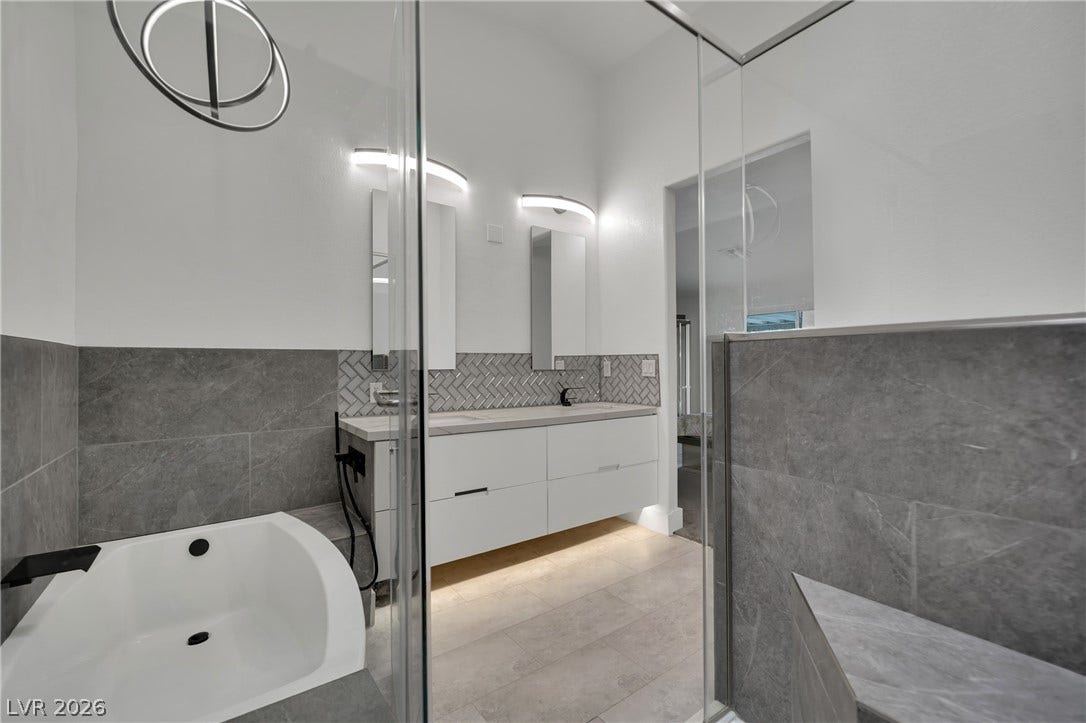 9180 Mohawk Street, Las Vegas, NV 89139 Full bathroom featuring tile walls, double vanity, a garden tub, wainscoting, and light tile patterned floors