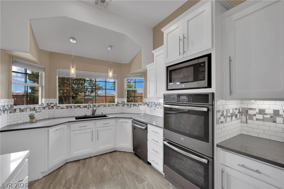 9180 Mohawk Street, Las Vegas, NV 89139 Kitchen with stainless steel appliances, double oven. white cabinetry, decorative backsplash, and hanging light fixtures