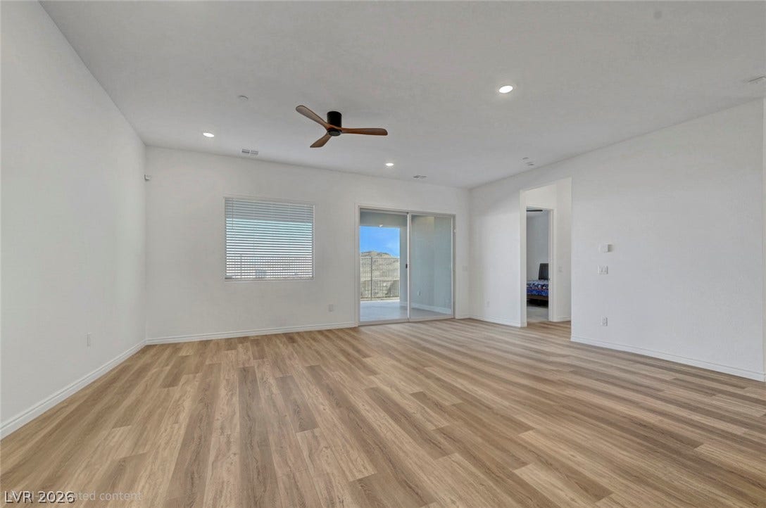 A spacious room offers comfortable living with warm wood-look flooring and a ceiling fan for climate control.