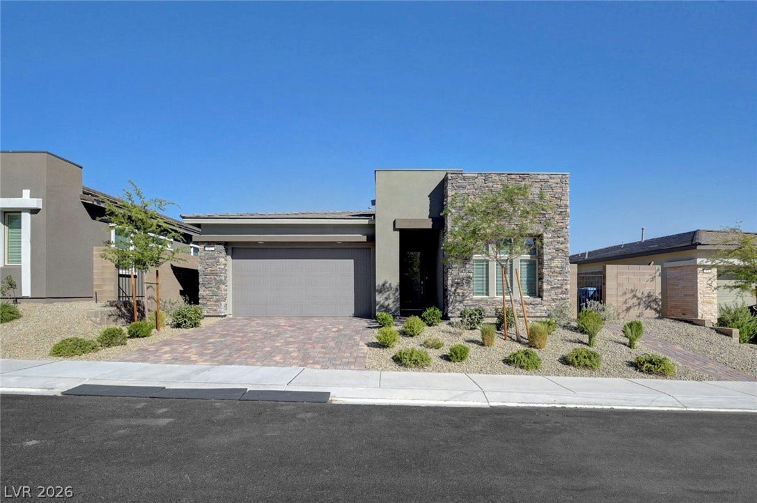 Modern desert landscaping and a paver driveway enhance this striking stone and stucco facade.