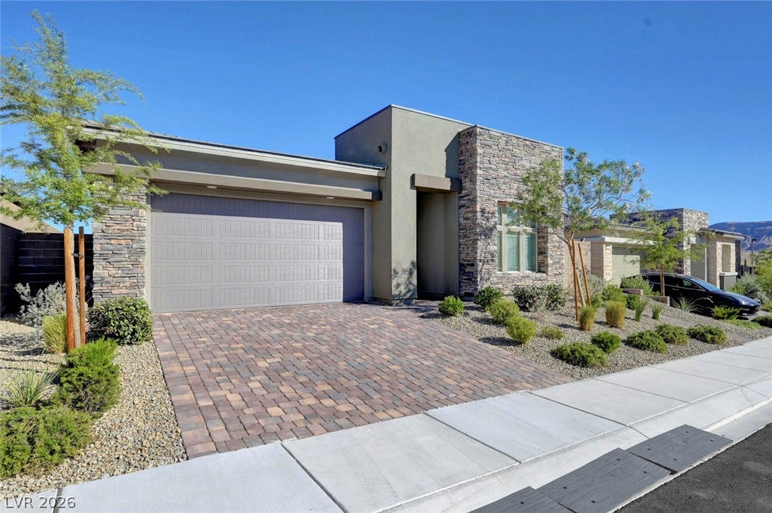 A well-maintained front yard offers lush landscaping and a paver driveway leading to an attached garage.