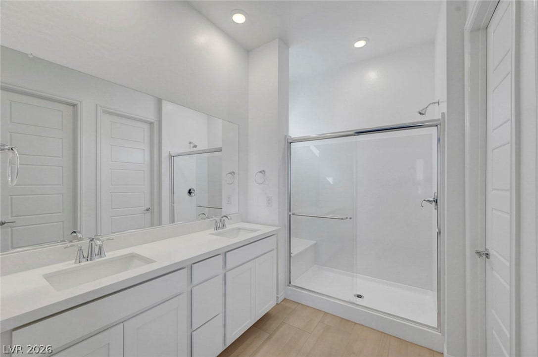 Dual vanities and a glass-enclosed shower create a practical, bright bathroom retreat.