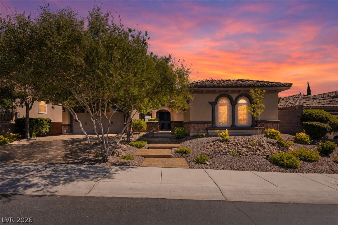 2397 Luberon Drive, Henderson, NV 89044 An inviting front facade with lush landscaping and a driveway, all under a colorful twilight sky.