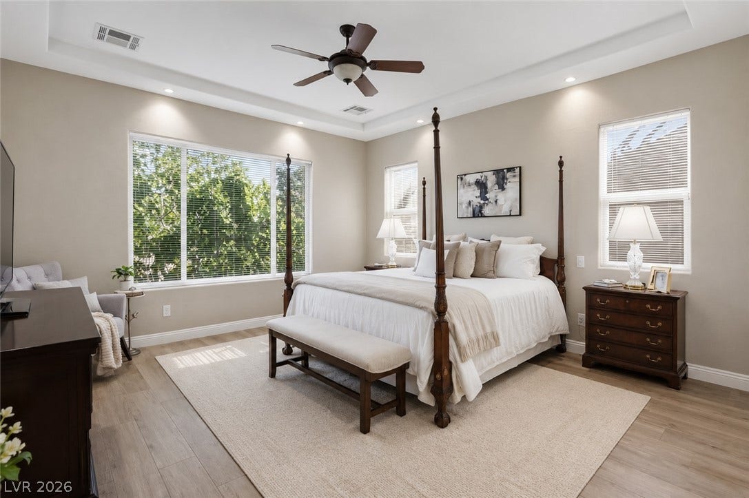 2397 Luberon Drive, Henderson, NV 89044 A tranquil primary bedroom with a soaring tray ceiling and recessed lighting, offering verdant views through large windows.