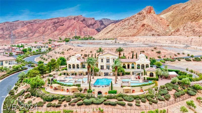 6 VIA VASARI, #102, Henderson, NV 89011 A desert oasis with a grand estate, multiple pools, and manicured landscaping, all against a dramatic mountain backdrop.