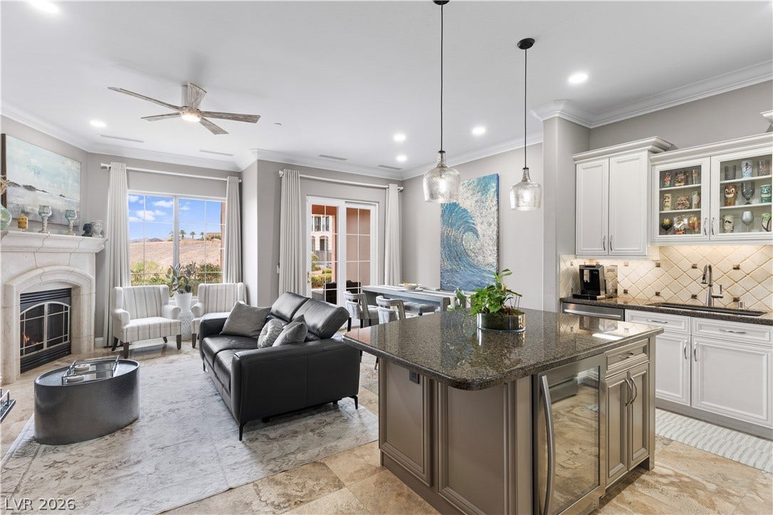6 VIA VASARI, #102, Henderson, NV 89011 An open-concept living area with a beautiful fireplace seamlessly connects to a kitchen featuring an island with pendant lighting.