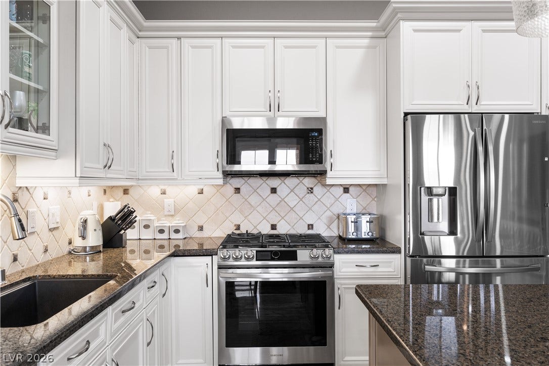 6 VIA VASARI, #102, Henderson, NV 89011 White cabinetry, granite counters, and stainless appliances define this well-appointed kitchen.