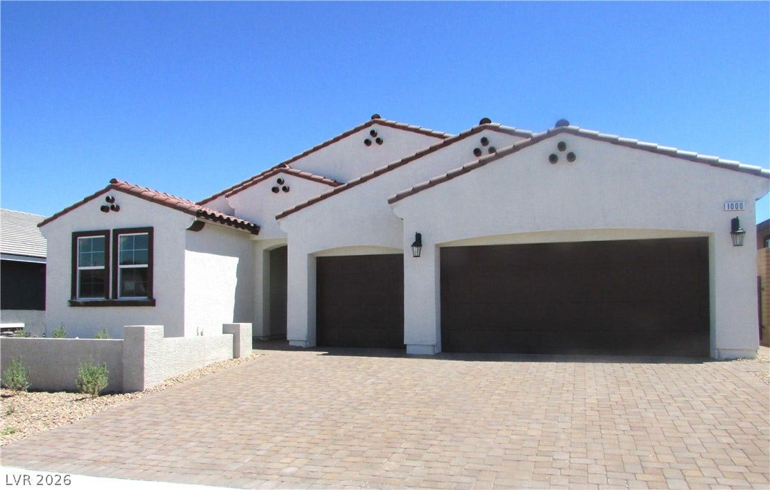 A spacious brick paver driveway leads to a modern stucco exterior with tile roof details. Photo is of actual home.
