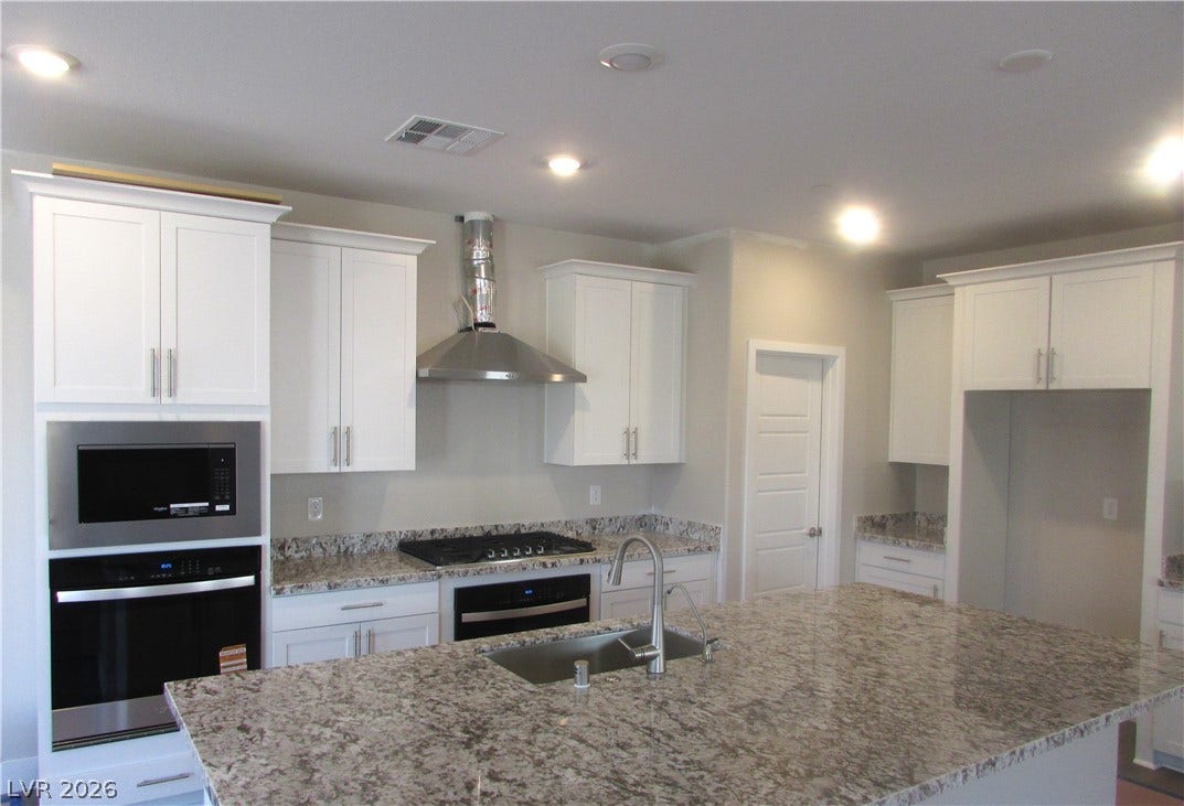 An expansive stone-topped island anchors this modern kitchen equipped with integrated stainless steel appliances. Photo is of actual home.
