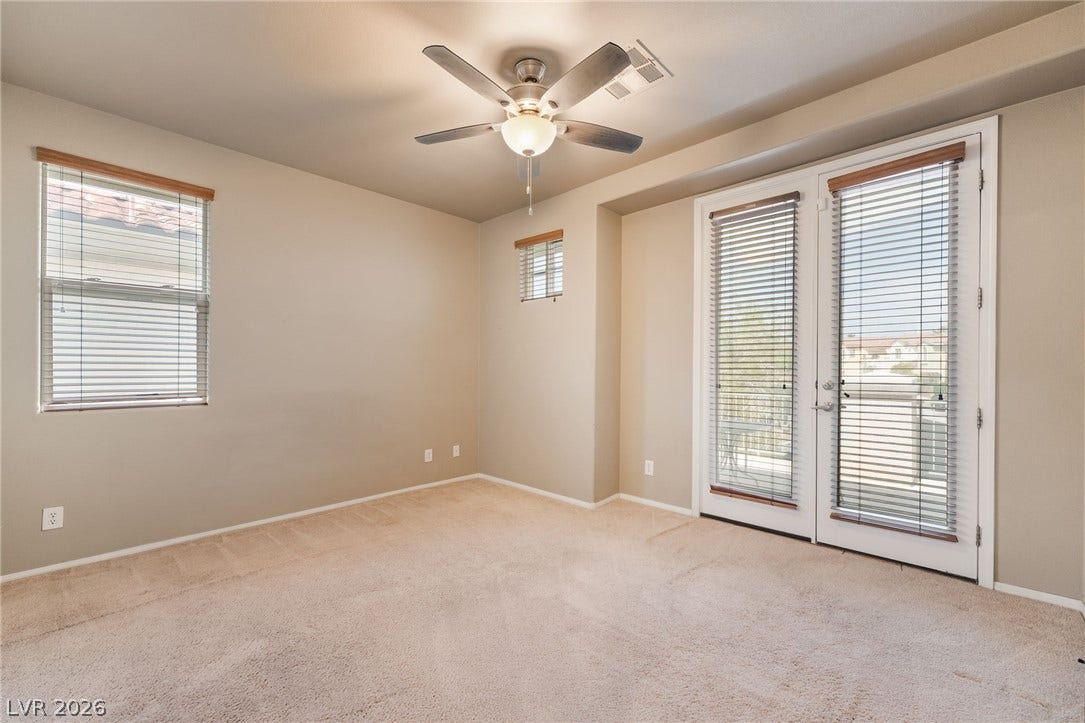 2439 Kaymin Ridge Road, Henderson, NV 89052 A comfortable bedroom features plush carpeting and access to outdoor space through French doors, illuminated by natural light and a ceiling fan.