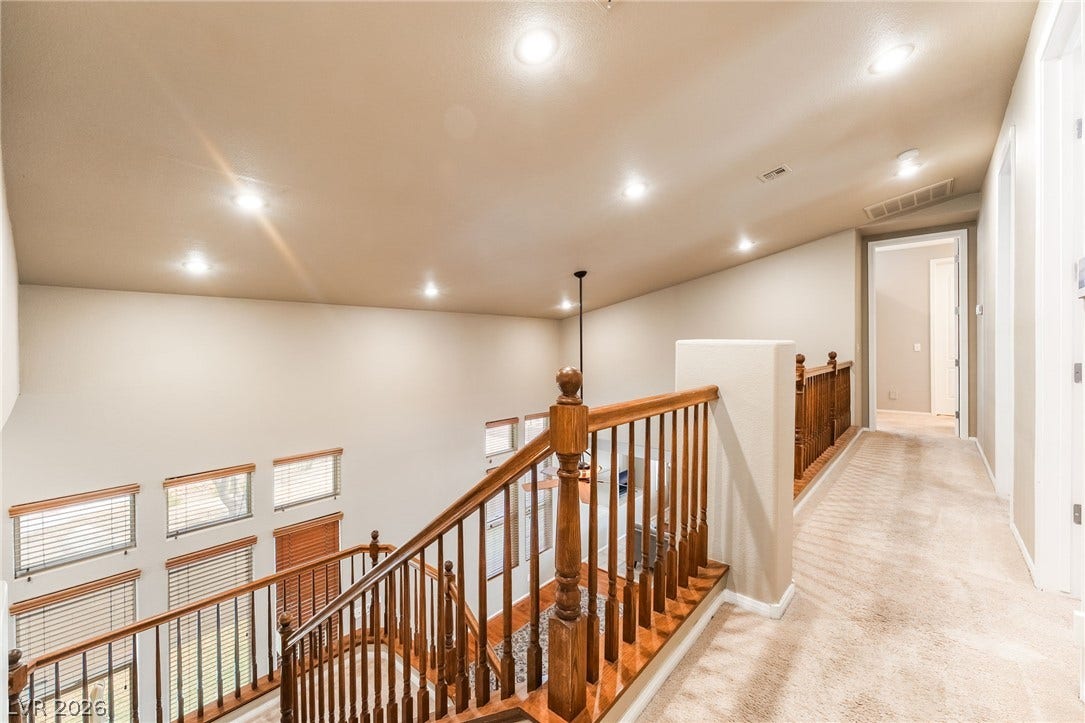 2439 Kaymin Ridge Road, Henderson, NV 89052 A grand wooden staircase with intricate banisters leads to a naturally illuminated upper landing and connecting hallway.