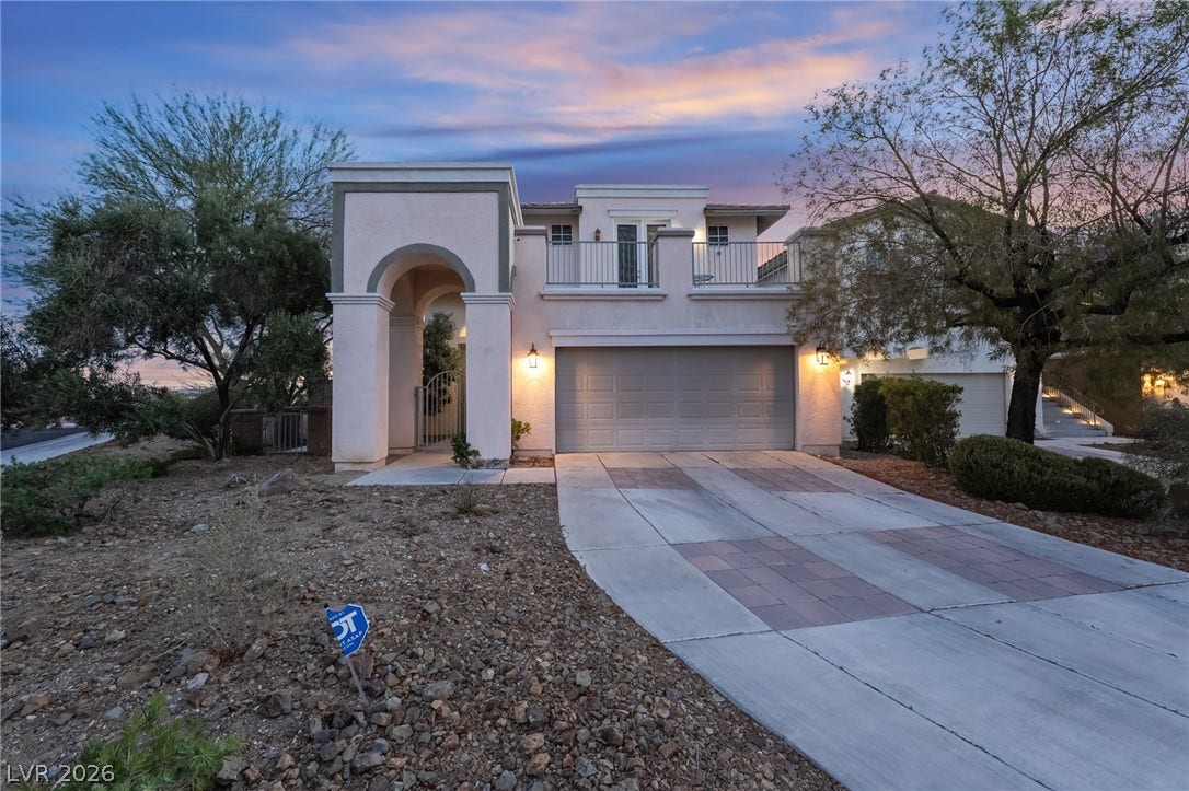 2439 Kaymin Ridge Road, Henderson, NV 89052 An inviting entry archway and dual balconies adorn this modern stucco residence with an integrated garage and a decorative paved driveway.