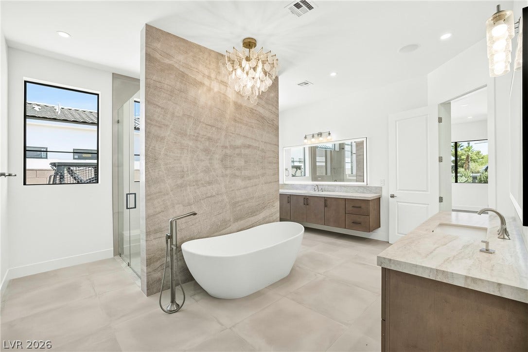 4360 Conough Lane, Las Vegas, NV 89129 A spacious, naturally illuminated primary bathroom offers a freestanding tub, separate glass-enclosed shower, and dual vanities with elegant countertops.