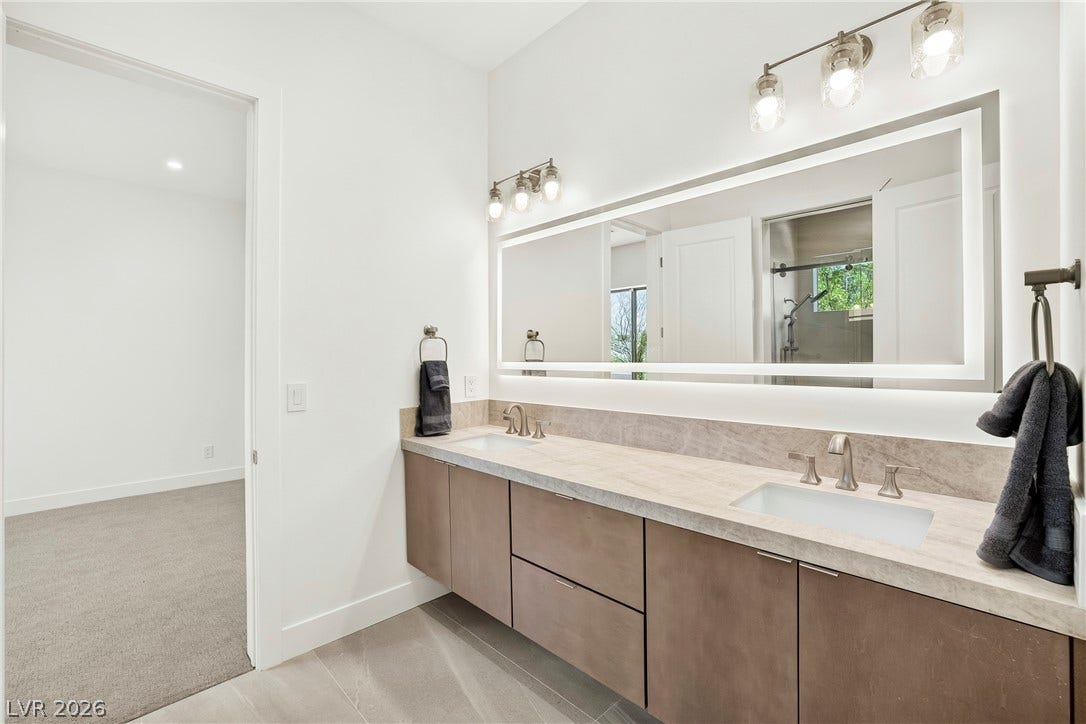 4360 Conough Lane, Las Vegas, NV 89129 A sleek dual vanity with stone countertops and an illuminated mirror anchors this contemporary bathroom design.