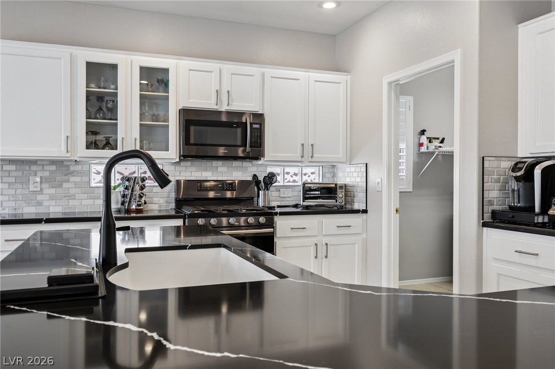 2141 Colvin Run Drive, Henderson, NV 89052 Modern kitchen with white cabinetry, black quartz countertops, and stainless steel appliances.