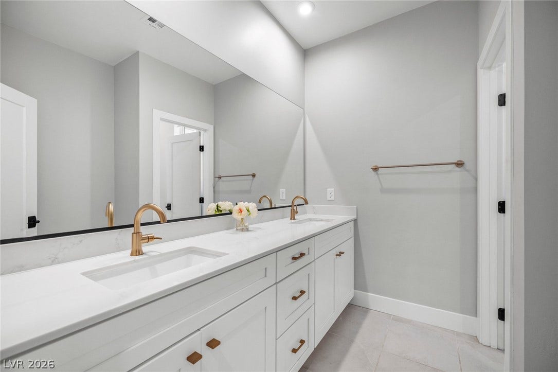 3194 Poplar Crest Court, Henderson, NV 89044 Double vanity with sleek white countertops and modern brass fixtures defines this well-appointed bathroom.
