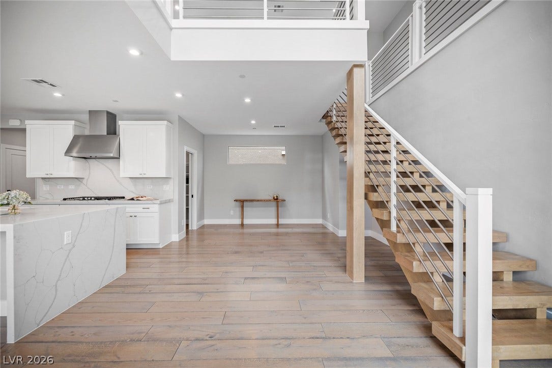 3194 Poplar Crest Court, Henderson, NV 89044 A grand staircase ascends beside an open-concept kitchen and naturally illuminated living space, all grounded by hardwood flooring.