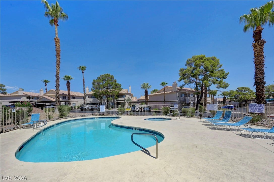 A refreshing community pool and spa await under the desert sky, surrounded by mature palm trees and lush landscaping.