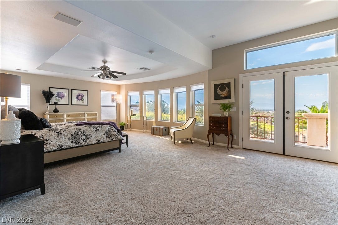 2676 Botticelli Drive, Henderson, NV 89052 A spacious primary bedroom retreat featuring a 2 sided fireplace, and access to the large balcony, The large windows all have gorgeous strip and city light views.