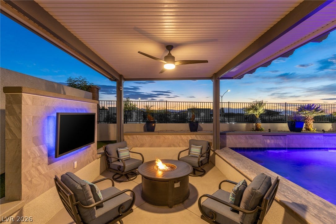 743 Glowing Horizon Street, Henderson, NV 89052 An inviting outdoor living space features a covered patio, fire pit, and illuminated pool, perfect for twilight relaxation.