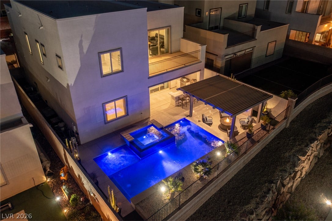 743 Glowing Horizon Street, Henderson, NV 89052 An illuminated backyard oasis boasts a sparkling pool, spa, and a cozy fire pit area under a covered patio.