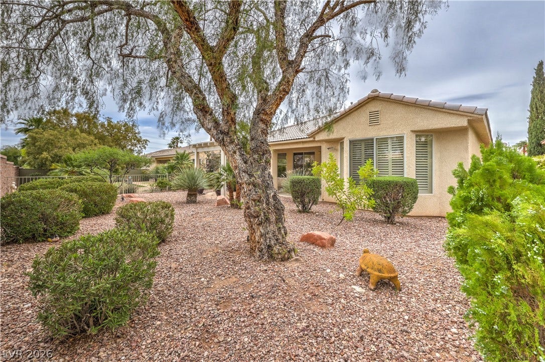 10298 Profeta Court, Las Vegas, NV 89135 A desert-friendly backyard featuring a gravel landscape with mature trees and lush shrubs.