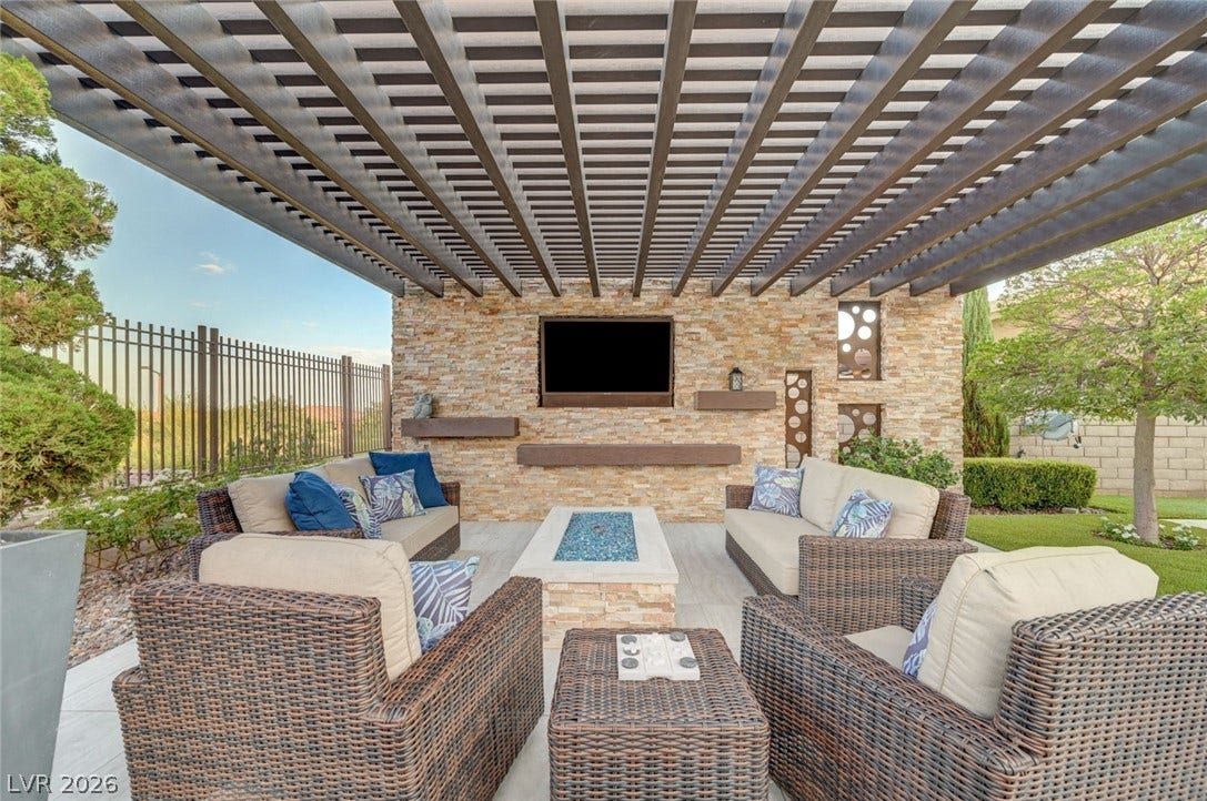 274 Evante Street, Las Vegas, NV 89138 An inviting covered patio featuring a natural stone wall, a modern fire pit, and comfortable wicker seating perfect for outdoor gatherings.
