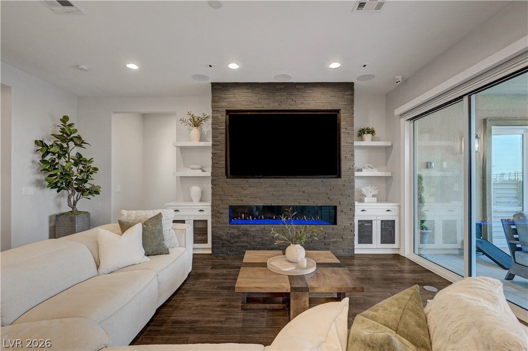 274 Evante Street, Las Vegas, NV 89138 An inviting living area features rich hardwood flooring and a stacked stone fireplace with an integrated modern flame display, offering seamless access to an outdoor patio.