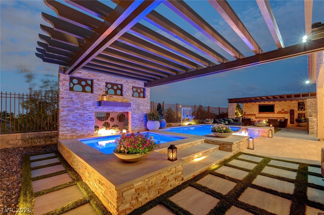274 Evante Street, Las Vegas, NV 89138 An illuminated backyard oasis presents a multi-level pool, spa, and fire feature, all under a modern pergola.