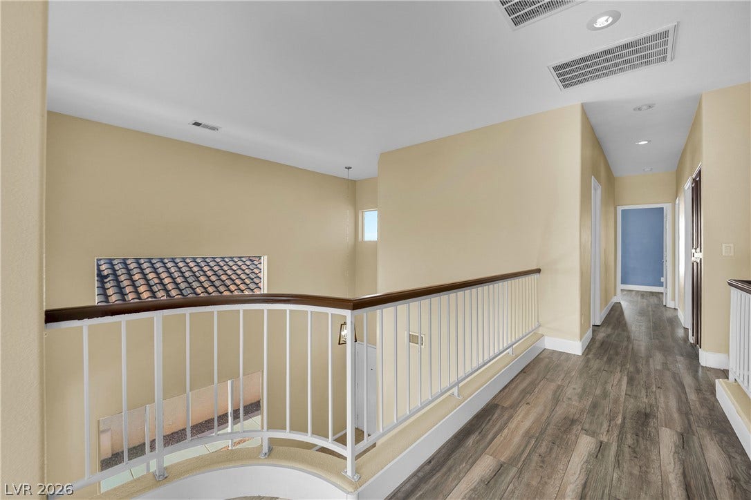 5823 Golden Wing Street, Las Vegas, NV 89113 A graceful staircase with a wrought iron railing descends from a sunlit upper landing featuring rich wood flooring.