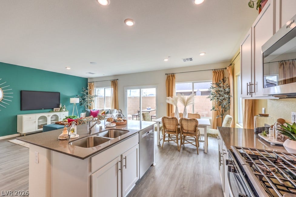 1090 Saffron Toucan Lane, Henderson, NV 89011 Kitchen featuring white cabinetry, open floor plan, appliances with stainless steel finishes, dark stone counters, and light wood-style flooring. Home is representational only; actual home finishes may vary.