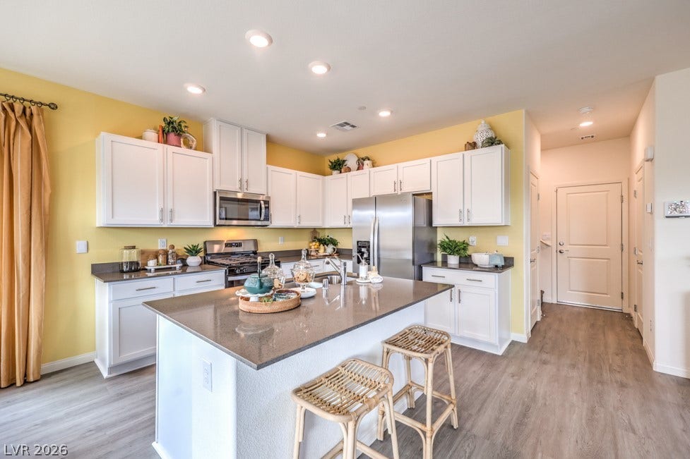 1090 Saffron Toucan Lane, Henderson, NV 89011 Kitchen featuring white cabinetry, dark stone countertops, appliances with stainless steel finishes, a breakfast bar, and light wood-style floors. Home is representational only; actual home finishes may vary.