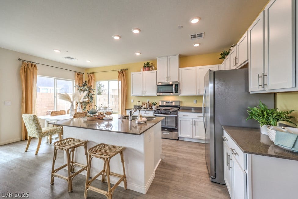 1090 Saffron Toucan Lane, Henderson, NV 89011 Kitchen featuring appliances with stainless steel finishes, a kitchen bar, a kitchen island with sink, light wood-style floors, and dark stone counters. Home is representational only; actual home finishes may vary.