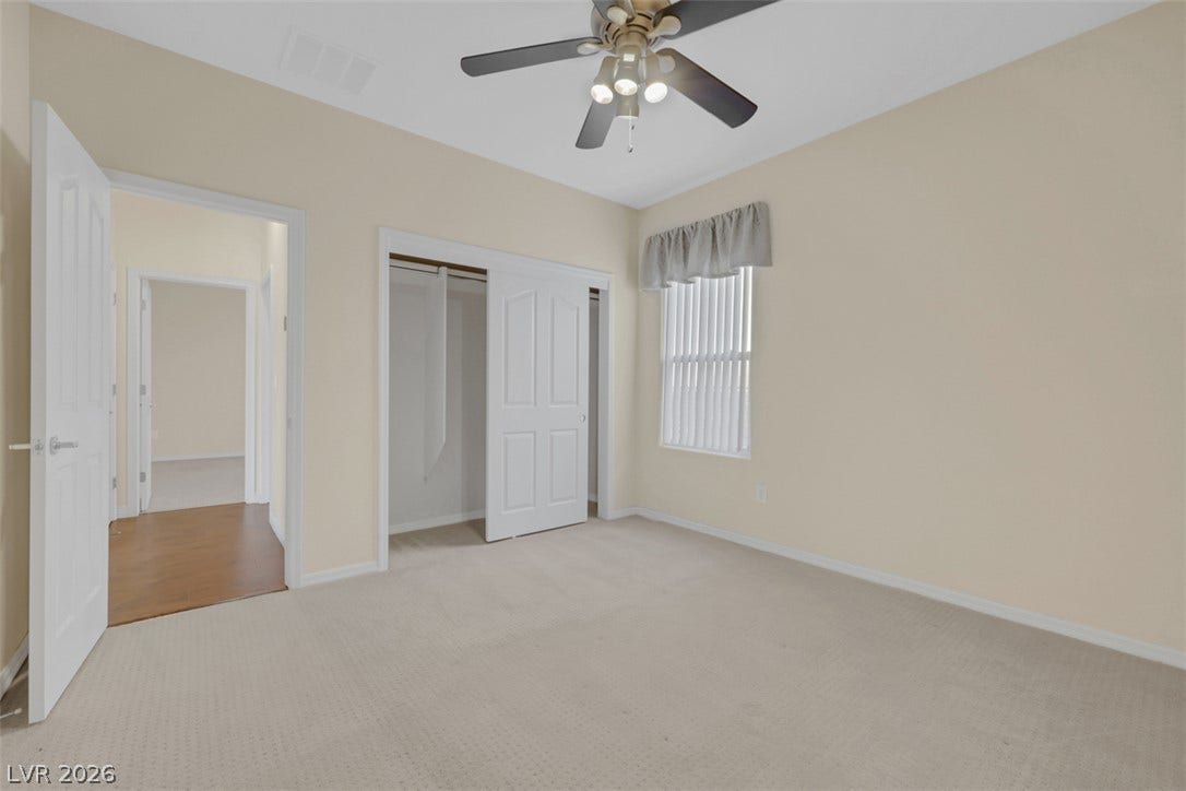 A well-proportioned room featuring a ceiling fan, plush carpeting, and ample natural light from a window with blinds.