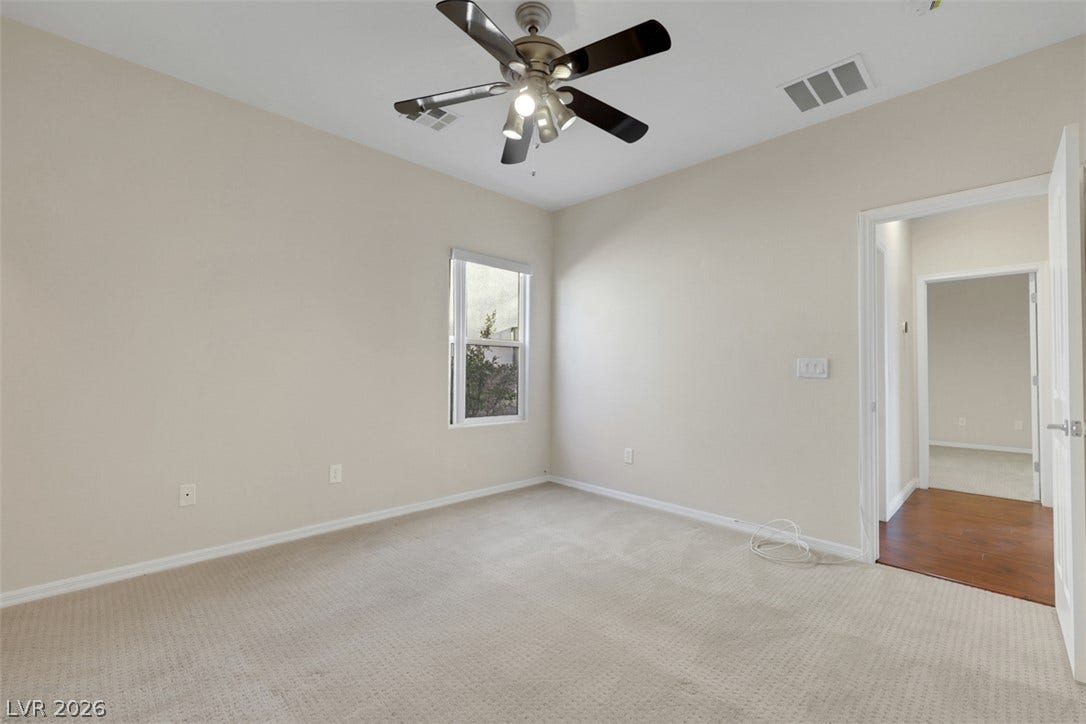 A well-proportioned bedroom features soft carpeting, a bright window, and a ceiling fan for comfort.