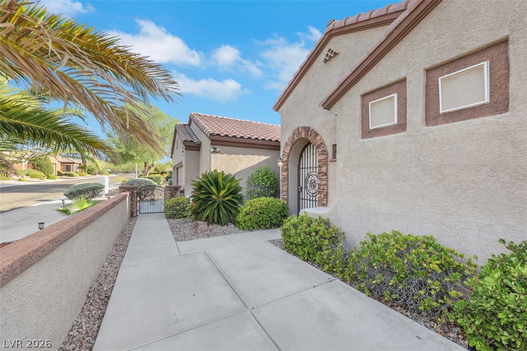 A terracotta-tiled roof crowns this stucco-sided residence, featuring an inviting arched stone entry and a gated side yard.