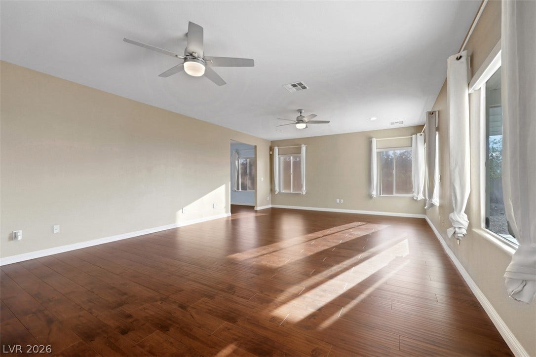 Sun-kissed engineered wood floors define this generously proportioned interior space, illuminated by multiple windows.