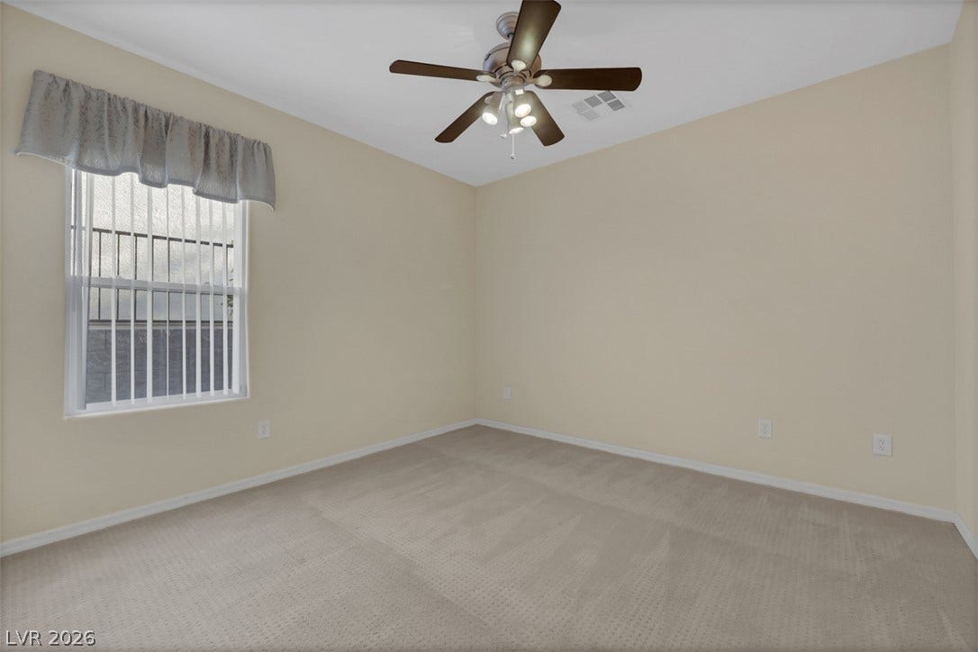A well-lit bedroom with soft carpeting and a functional ceiling fan.