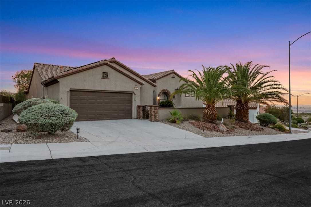 Elegant stucco facade welcomes with a spacious driveway and desert landscaping under a vibrant sunset.