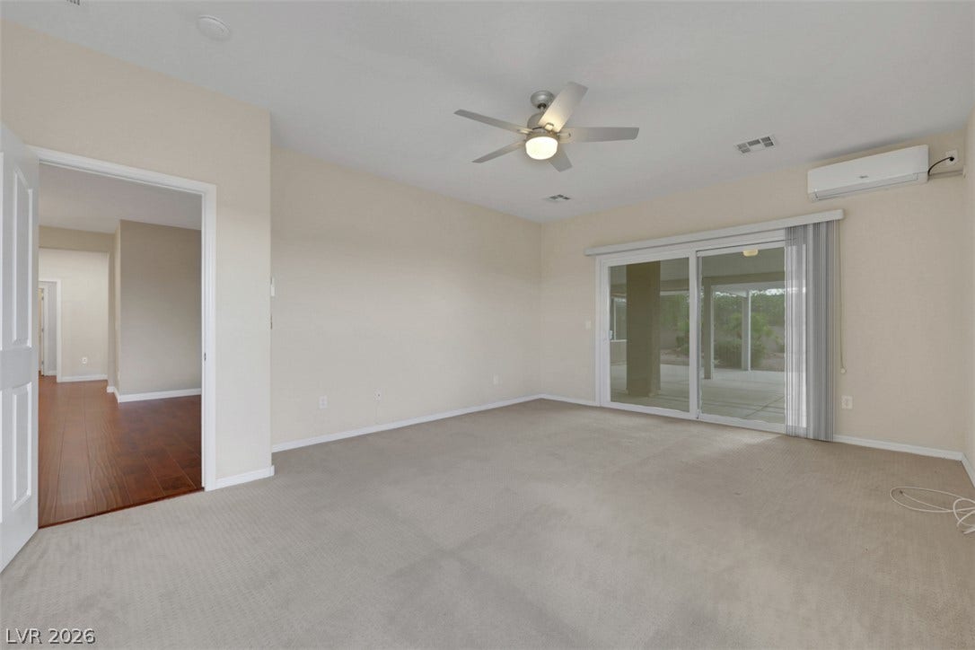 A spacious room with carpeted floors and a modern ceiling fan opens to an outdoor covered patio via large sliding glass doors.