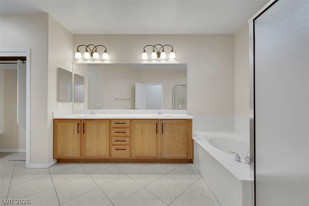 A well-lit primary bathroom featuring dual vanities, an ample mirror, and a pristine soaking tub.