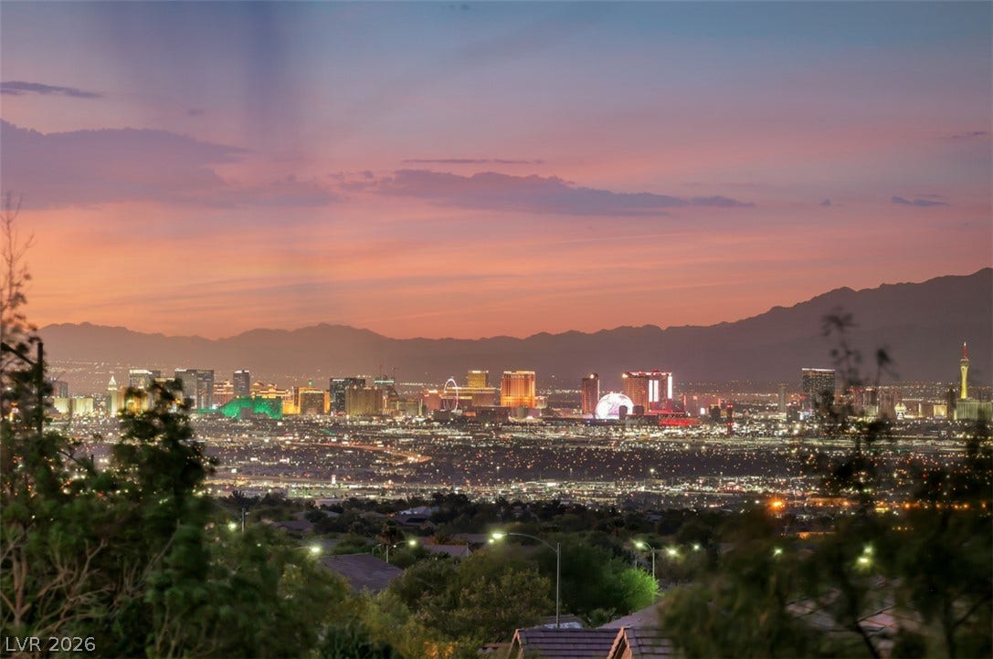Vibrant city lights illuminate the desert horizon beneath a colorful twilight sky.