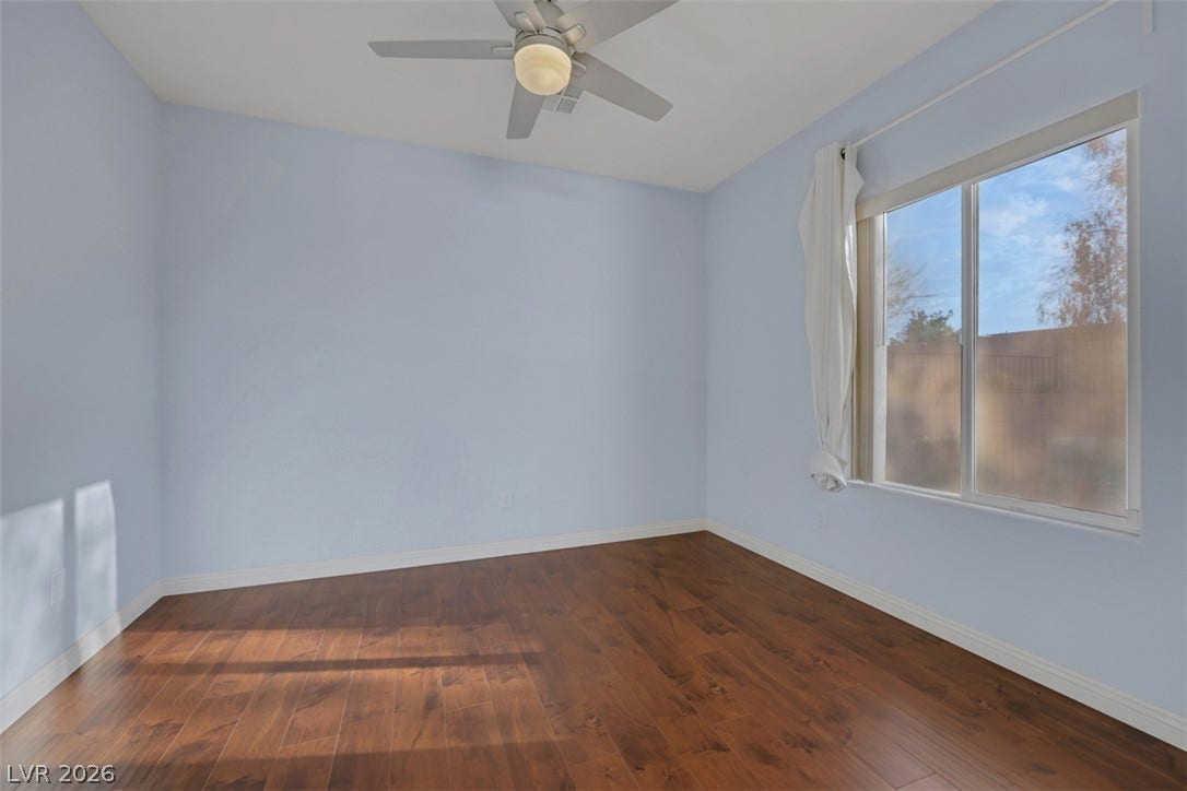 A quiet bedroom showcases a bright window and rich hardwood flooring, ready for personalization.