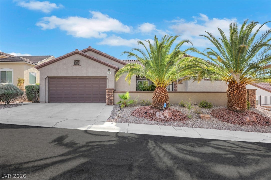 A desert oasis welcomes you with a stucco exterior, a large driveway, and lush palm trees.