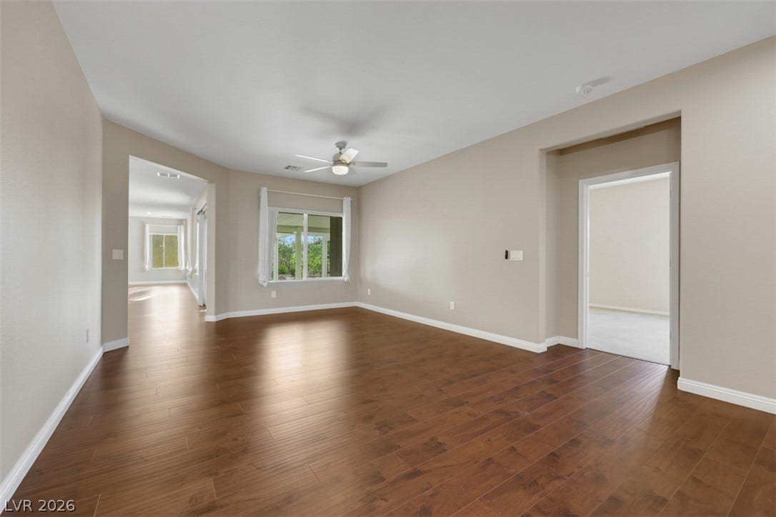 Rich hardwood floors extend through this generously proportioned living space, illuminated by natural light and overhead fan.